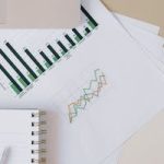 Flat lay of a workspace featuring a laptop, graphs, and a notebook for financial analysis.